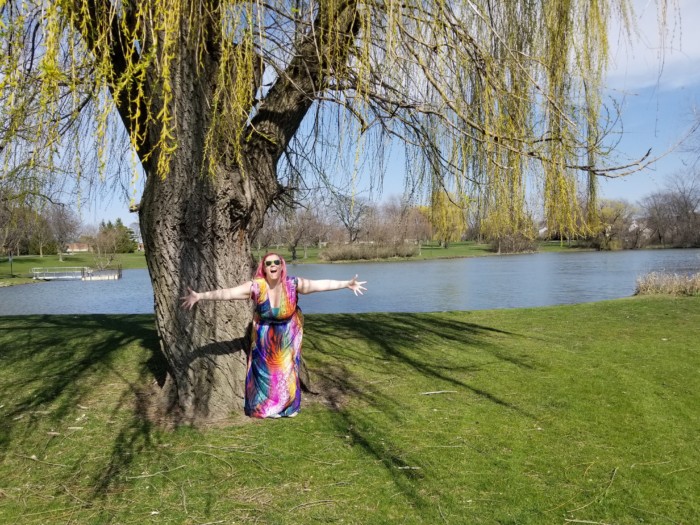 Chrissy wearing a brightly colored patterned dress in front of a willow tree and a lake