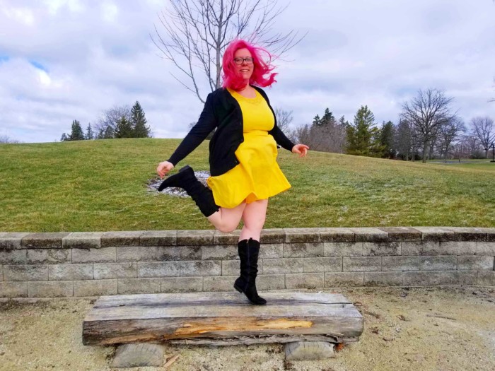 Chrissy dancing on a bench with pink hair and a yellow dress
