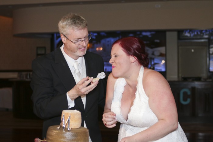 hilarious professional wedding photos  laughing while cutting the cheese wedding cake made of cheese wheels