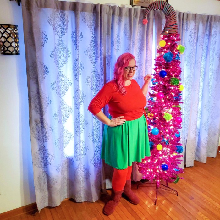Chrissy in front of a pink Christmas tree wearing red and green